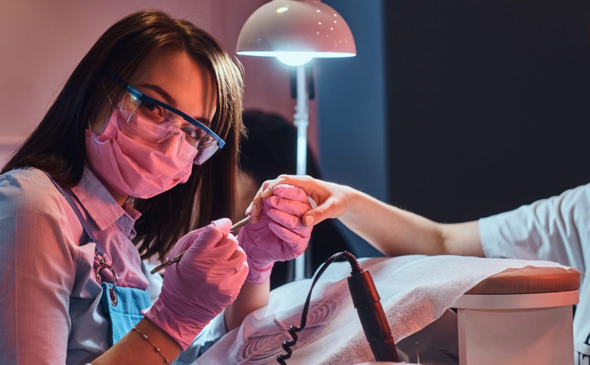 beautiful-cheerful-manicure-master-is-looking-camera-while-working-client-s-nails (1)